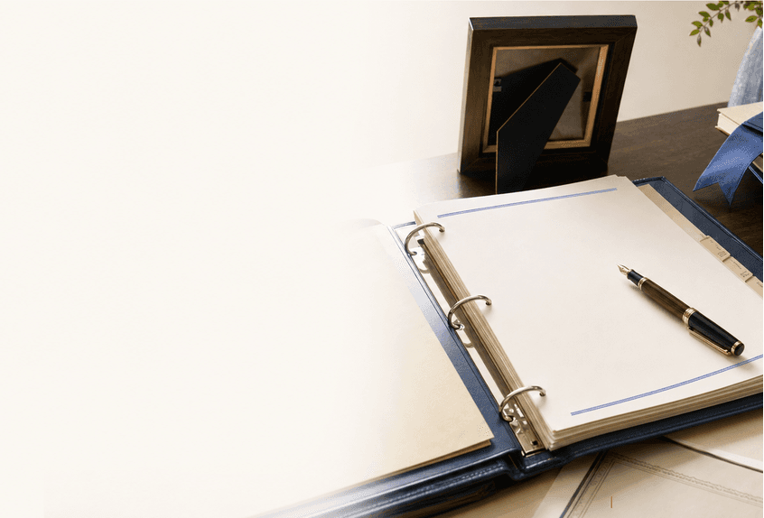 An estate binder, trust documents, and a fountain pen arranged on a private-office desk beside a turned-away photo frame